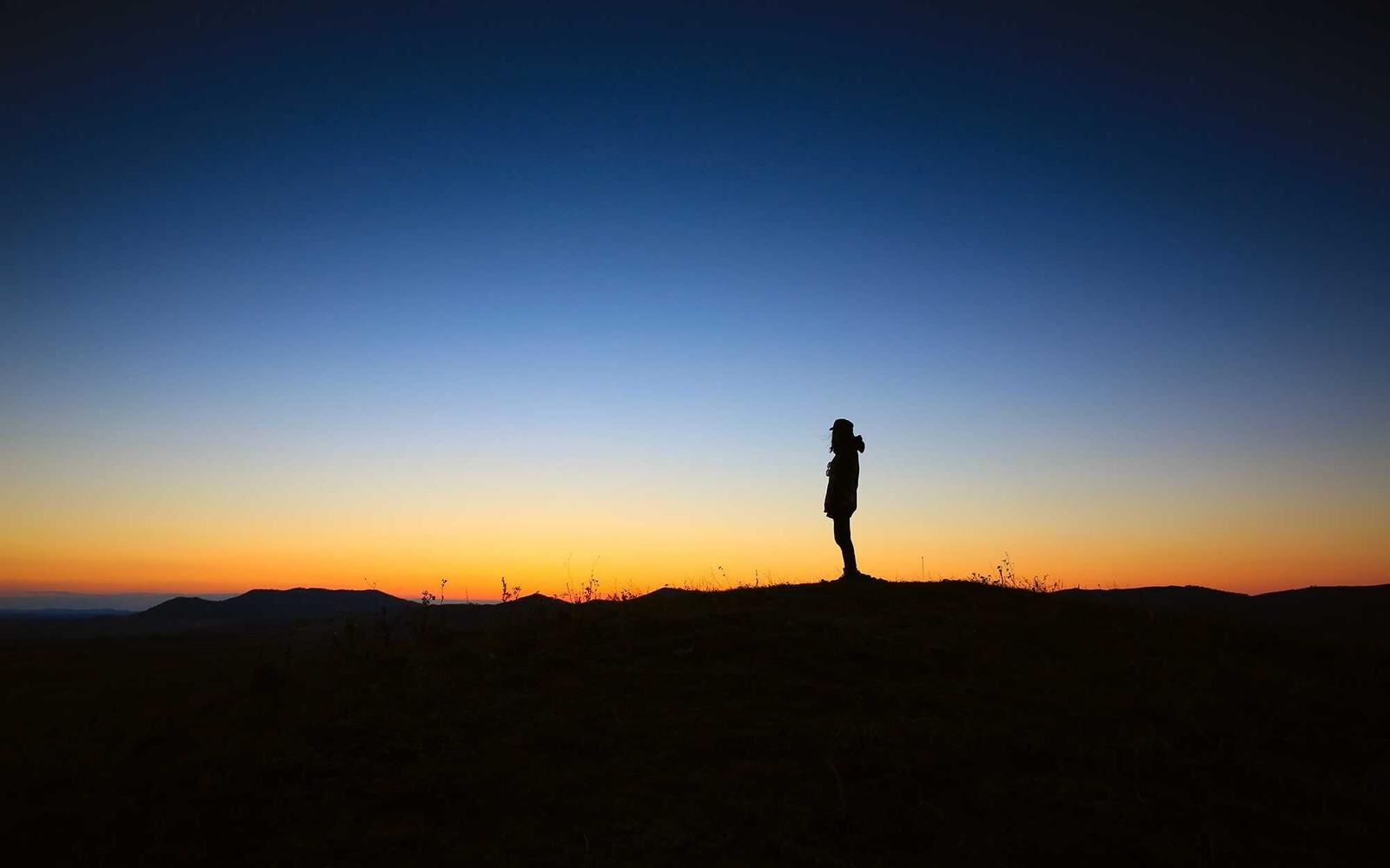 A figure on a dark ridge under a blue and orange sky before dawn