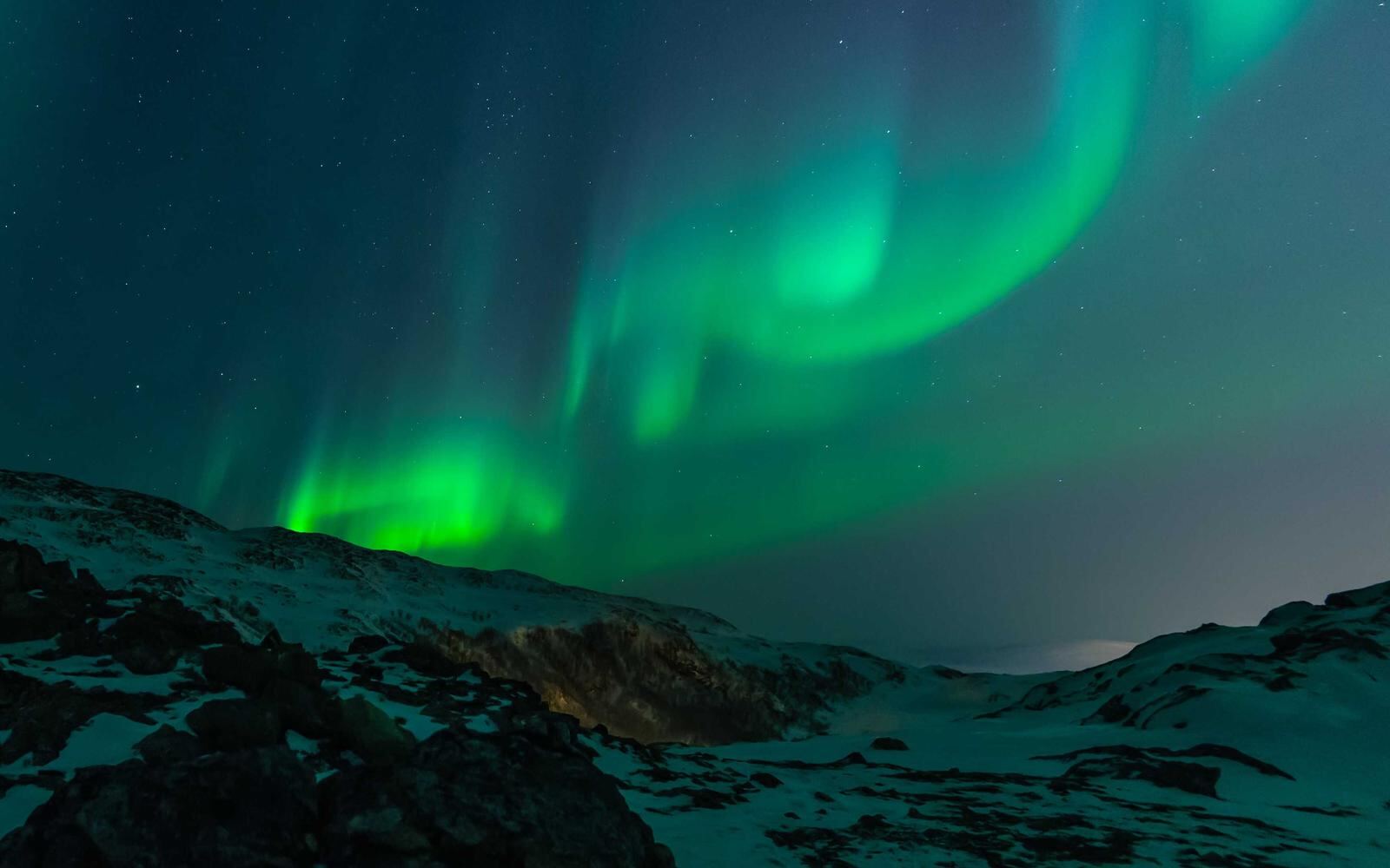 Green aurora over snowy hills at night